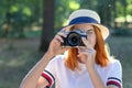 Pretty teenage girl with red hair taking picture with photo camera in summer park Royalty Free Stock Photo