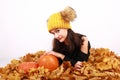 Girl in cap with bobbles lying on autumn leaves by pumpkins Royalty Free Stock Photo