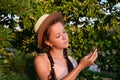 pretty teenage girl in summer dress and hat holds pine cone in her hand. Portrait of girl on background of green park in rays of Royalty Free Stock Photo