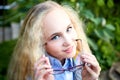 Pretty teenage girl 14-16 year old with curly long blonde hair and in glasses in the green park in a summer day outdoors. Royalty Free Stock Photo