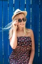 Cute teenage hipster girl smiling in straw hat, dress and sunglasses outdoor over blue wooden background. Royalty Free Stock Photo
