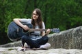 Pretty teenager girl playing guitar while sitting on the stone bridge