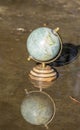 Pretty terrestrial globe in wood and metal, placed in a puddle outside, and its reflection