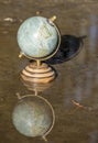 Pretty terrestrial globe in wood and metal, placed in a puddle outside, and its reflection