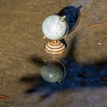 Pretty terrestrial globe in wood and metal, placed in a puddle outside, and its reflection