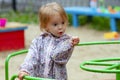 Pretty toddler girl wearing rain jacket playing on the karusel on the playground