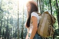 Pretty traveling woman with backpack and hat standing in forest. Young hipster girl walking among trees on sunset