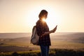 Pretty traveling woman standing on top of mountain at sunset and using mobile phone
