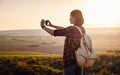 Pretty traveling woman standing on top of mountain at sunset and using mobile phone