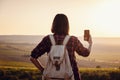 Pretty traveling woman standing on top of mountain at sunset and using mobile phone