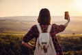 Pretty traveling woman standing on top of mountain at sunset and using mobile phone