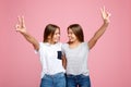 Pretty two young twin sisters with beautiful smile with hands up showing peace gesture over pink background. Royalty Free Stock Photo