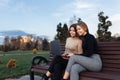 Pretty two young twin sisters in casual outfit with bright smile use notebook or laptop on bench at the park Royalty Free Stock Photo