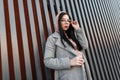 Pretty urban stylish young woman hipster in fashionable long gray coat straightens fashion glasses near vintage metal wall in the Royalty Free Stock Photo