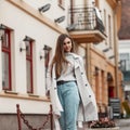 Pretty urban young woman with brown hair in elegant stylish trench coat walks outdoors in the city. Cute beautiful stylish girl Royalty Free Stock Photo