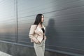 Pretty urban young woman in fashionable oversized leather beige jacket in stylish jeans walks near vintage building in the city. Royalty Free Stock Photo