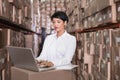 Asian woman wearing white shirt working in warehouse scanning barcodes on boxes using silver laptop Royalty Free Stock Photo