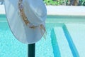 Pretty white beach hat hanging on pool fence. Royalty Free Stock Photo