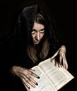 Pretty witch casts spells from thick ancient book by candlelight on a dark background Royalty Free Stock Photo