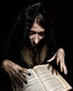 Pretty witch casts spells from thick ancient book by candlelight on a dark background Royalty Free Stock Photo