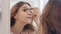 Pretty woman applying mascara with brush on eyelashes in bathroom mirror Royalty Free Stock Photo