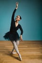 Pretty woman ballerina in tutu and pointe in black swimsuit posing in studio on blue background Royalty Free Stock Photo