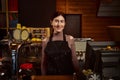 Pretty woman barista in apron behind the bar in a wooden cafeteria