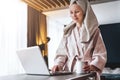 Pretty woman in bathrobe using laptop at table with partner in background at home in the kitchen Royalty Free Stock Photo