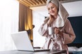 Pretty woman in bathrobe using laptop at table with partner in background at home in the kitchen Royalty Free Stock Photo