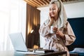 Pretty woman in bathrobe using laptop at table with partner in background at home in the kitchen Royalty Free Stock Photo