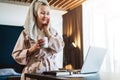 Pretty woman in bathrobe using laptop at table with partner in background at home in the kitchen Royalty Free Stock Photo