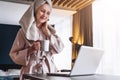 Pretty woman in bathrobe using laptop at table with partner in background at home in the kitchen Royalty Free Stock Photo