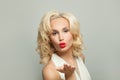 Pretty woman with blonde curly hair blowing kiss, fashion portrait