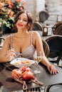 Pretty woman with candid smile laughing sitting at summer cafe, dressed in white printed dress, fashionable street style