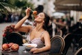 Pretty woman with candid smile laughing sitting at summer cafe, dressed in white printed dress, fashionable street style Royalty Free Stock Photo