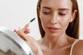 Pretty woman combing her eyebrows with brush and looking at mirror over white studio background Royalty Free Stock Photo