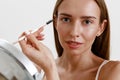 Pretty woman combing her eyebrows with brush and looking at mirror over white studio background Royalty Free Stock Photo