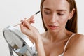 Pretty woman combing her eyebrows with brush and looking at mirror over white studio background Royalty Free Stock Photo