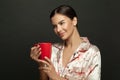 Pretty woman with cup of coffee. Beautiful adult female model hods in her hands red mug with hot drink in the morning