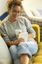 Pretty woman enjoy relax at home reading a book on tabler reader and drinking a tea or coffe sitting on a yellow sofa in living