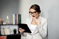 Pretty woman in formal outfit and glasses expressing surprise emotion while using tablet. Reading shocking news or e-mail.