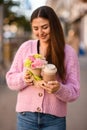 pretty woman gently holds flower arrangement in small pot and paper cup of coffee in her hands.