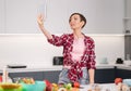 Pretty woman happy taking selfie using her smartphone at her new home while cooking fresh salad wearing a plaid shirt Royalty Free Stock Photo