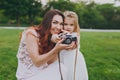 Pretty woman in light dress and little cute child baby girl take picture on retro vintage photo camera in park. Mother Royalty Free Stock Photo