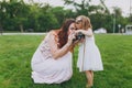 Pretty woman in light dress and little cute child baby girl take picture on retro vintage photo camera in park. Mother Royalty Free Stock Photo