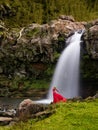 Pretty woman in long red dress enjoys the wet breeze of the nature under a waterfall in Azores.