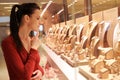 Pretty woman looking at jewelry in store window. Customer near jewellery. Dreamy long haired girl chooses silver, gold, diamonds,