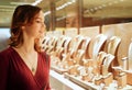 Pretty woman looking at jewelry in store window. Smiling interested customer near jewellery. Girl chooses gold, diamonds or