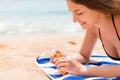 Pretty woman is lying on the towel at the beach and opening a tube of sun cream to protect her skin from sunburn Royalty Free Stock Photo