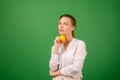 A pretty woman of middle age in a white shirt holds an apple in her hand on a green background. Healthy eating, vegetarianism, Royalty Free Stock Photo